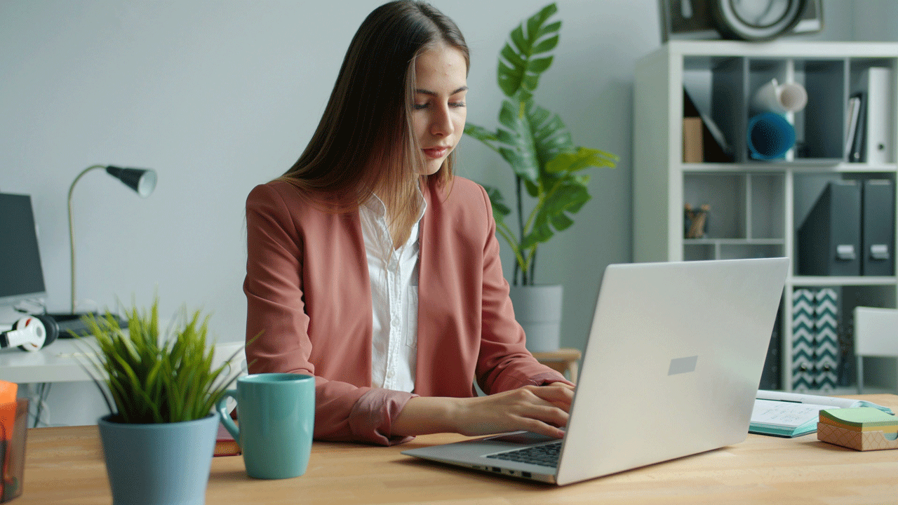 young woman sitting at the desk, typing on laptop